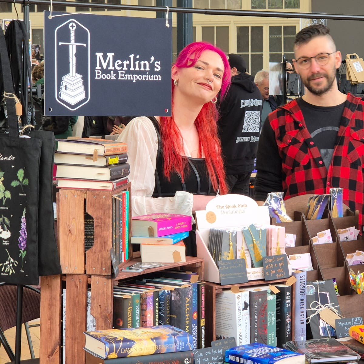 Two people standing behind a table filled with books at Merlin's Book Emporium.