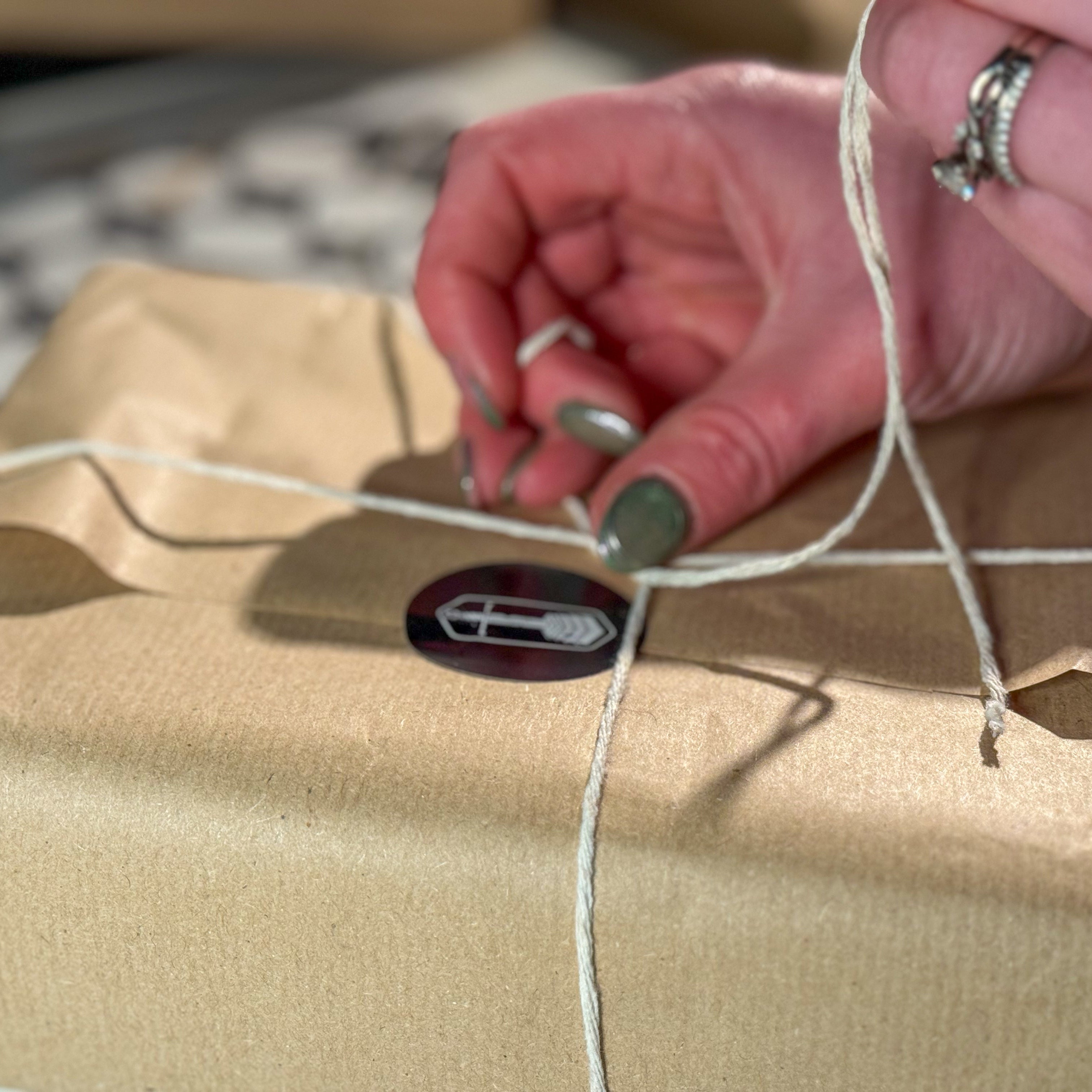 Person tying a string on a wrapped package with a visible brand logo.
