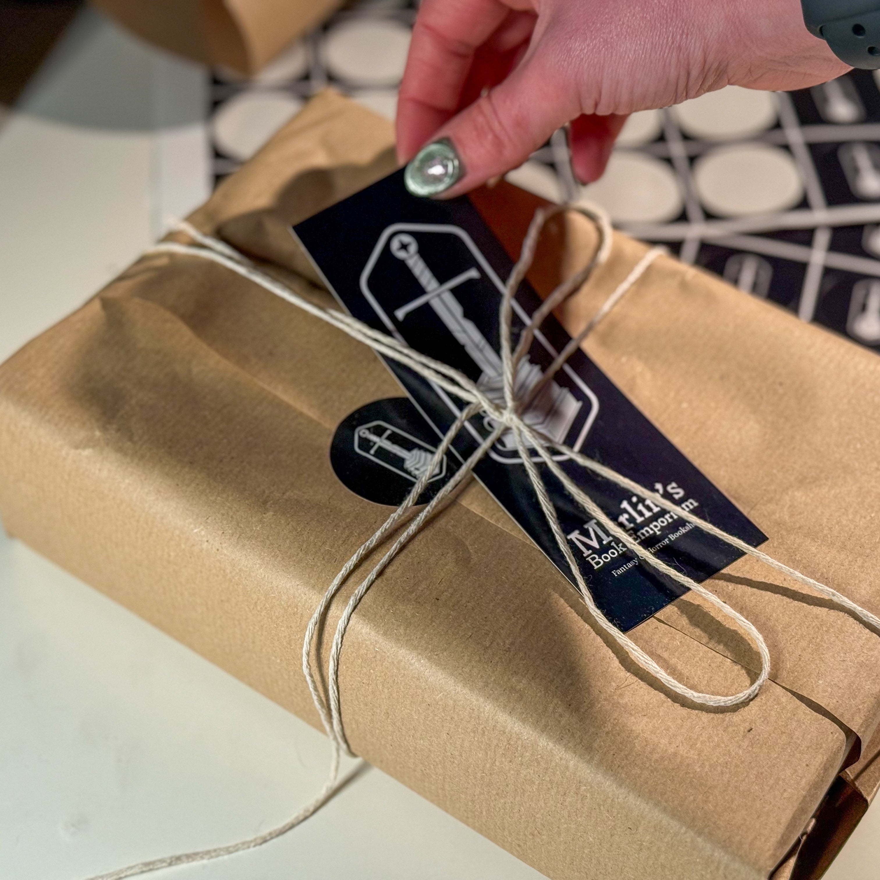 Gift box wrapped in brown paper with a label being attached, on a light surface.