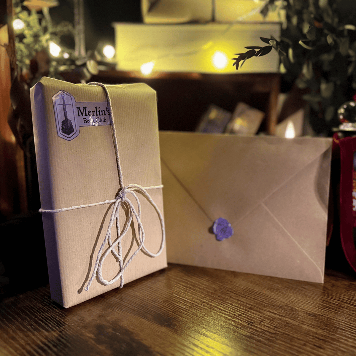 A wrapped package tied with twine and a matching envelope with a purple wax seal, styled on a wooden surface with warm string lights in the background. A label on the package reads 'Merlin's'.